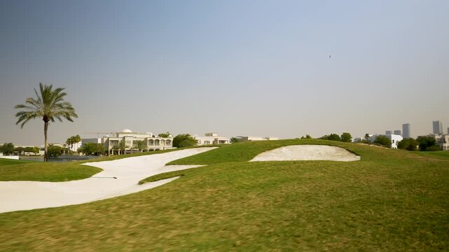 Scenic view of a golf course with palm trees, manicured lawns, and modern buildings in the background, showcasing a sunny day