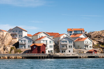 Waterfront apartment buildings at Hamnpromenaden, Kungshamn, Bohuslän, west coast Sweden, with red boathouses, wooden boardwalk and rocky shoreline © TasfotoNL