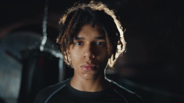 Handsome black guy looking at camera in gym, portrait of professional sportsman. Stylish guy with dreadlocks do sports in modern fitness club, box fighter preparing to workout, motivated athlete