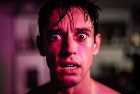 A man with an intense, fearful expression. He is drenched and appears to be experiencing a moment of extreme distress. A dimly lit interior space.