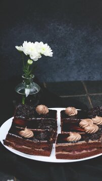 Decadent chocolate cake slices with cream frosting and white flowers on a dark background