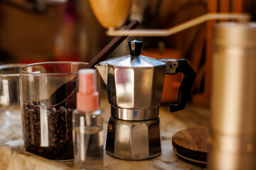 Moka pot on the table at home. Coffee making concept.  Moka pot, bean spray, coffee grinder, jar of coffee beans standing on the kitchen table.