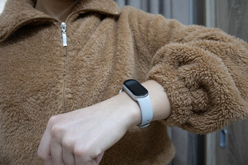 Close-up focus on the texture of a brown fleece jacket and a grey fitness tracker worn on a woman's wrist © Iuliana
