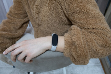 Detailed shot of a woman's hand resting on a chair, wearing a grey fitness tracker and a cozy brown teddy fleece jacket. © Iuliana