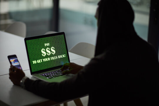 Hacker, person or laptop screen with phone in office for ransomware, data theft or payment demand. Extortion, tech or criminal with cybercrime at company for fraud, encryption or ransom note at night