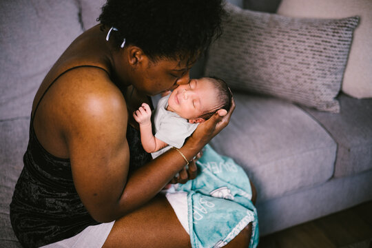 Mother snuggling with newborn baby boy at home on couch