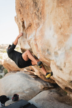 Young climber scaling overhanging boulder in Joshua Tree desert