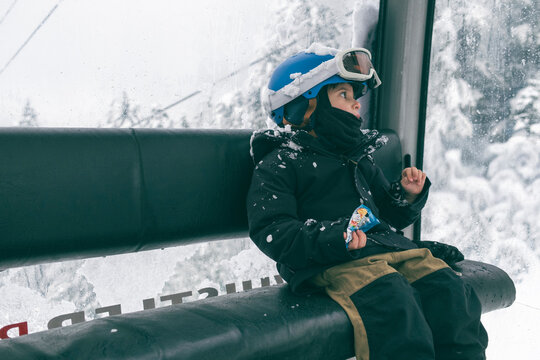 You boy snowboarder rides gondola and has a snack on winter day