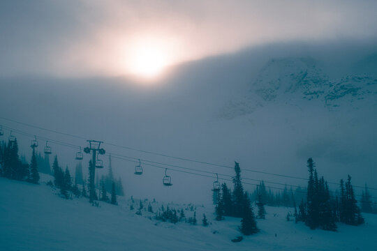 Sun shines through fog on chairlift at ski resort in winter