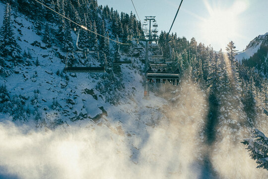 Skiers ride chairlift over snow gun on sunny day at Whistler