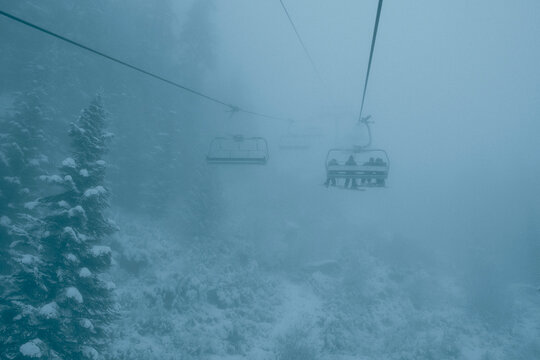 Snowboarders ride chairlift on stormy foggy day at whistler.