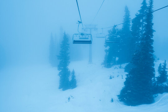 Snowboarders ride chairlift on stormy foggy day at whistler.