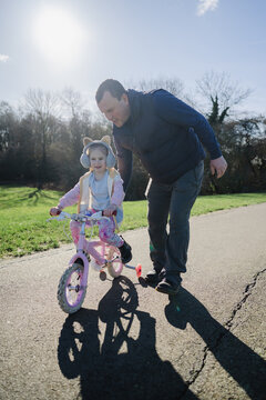 Father teaching his daughter riding a bicycle in the park