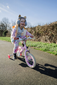 Little girl riding a pink bike in the park with her family