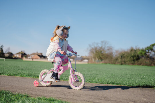 Little girl riding a pink bike in the park with her family