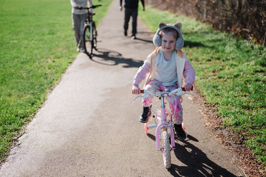 Little girl riding a pink bike in the park with her family