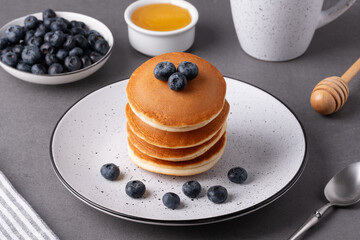 Pancakes with blueberries and honey on a grey table during breakfast time in a cozy kitchen setting