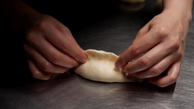 Closeup of hands carefully folding and sealing delicate dough to form a handmade dumpling on a metal surface in a low light artisan kitchen setting