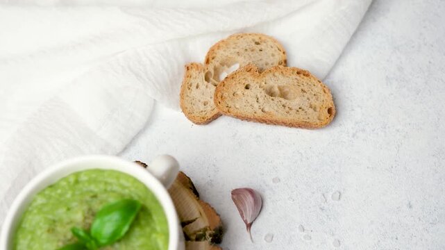 Green soup with basil, crusty bread slices and garlic clove on textured surface
