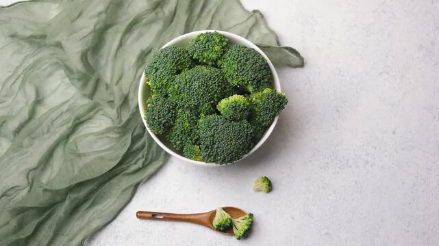 Fresh green broccoli florets in a white bowl with a wooden spoon on a light textured surface.