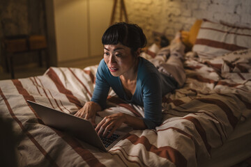 Fototapeta premium Woman smiling and laughing while watching laptop in bed