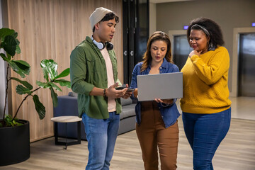 Diverse coworkers in casual attire discussing project while reviewing laptop and phone in lounge