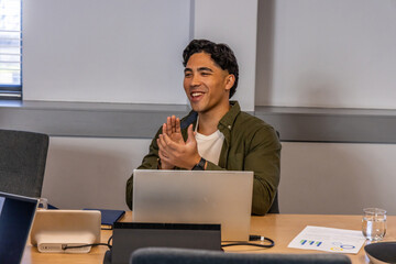 Man sitting at conference table, clapping and smiling while using silver laptop with notebook © wavebreak3