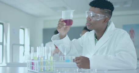 Inspecting student wearing white lab coat and goggles, holding red beaker in school lab, copy space © vectorfusionart