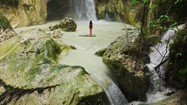 Drone tilts up showing woman facing brownish waterfall after typhoon in Cebu