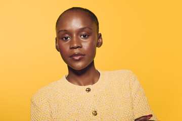 Confident African woman with dark skin wearing a yellow textured sweater stands with arms crossed against a bright yellow background. Concept for empowerment, fashion, and beauty. © SHOTPRIME STUDIO