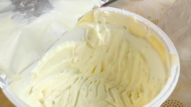 A woman takes sour cream from a container with a fork. Sour cream dried at the edges of the container. butter