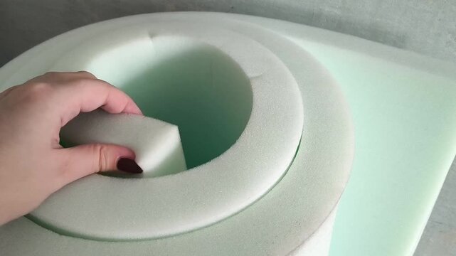 A woman's hand touches the soft foam rubber close-up. A roll of foam rubber for upholstery of upholstered furniture, sofa. Insulation