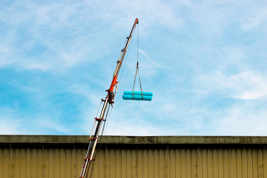 Industrial telescopic crane lifting heavy cargo wrapped in blue plastic against a bright sky, construction site and heavy machinery concept.
