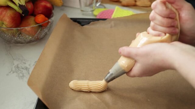 Woman piping cream onto baking sheet in sunny kitchen. Making custard cakes with pastry bag. Home baking process for desserts and pastries. video footage video footage photography
