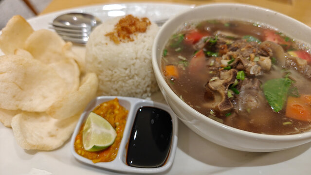 Indonesian Oxtail Soup or Sop Buntut Served with Steamed Rice Crackers and Chili Sambal - Authentic Culinary Heritage