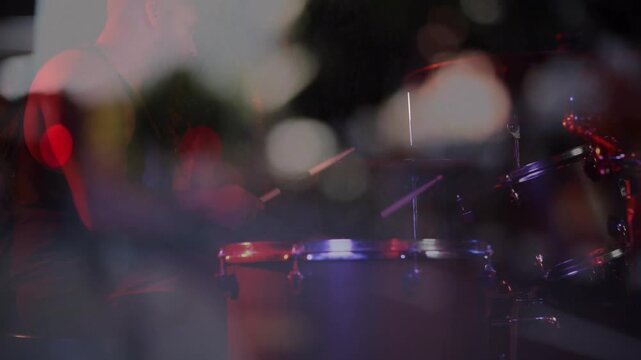Stage lights moving, low camera shifting focus, revealing drum kit with bokeh, highlighting music