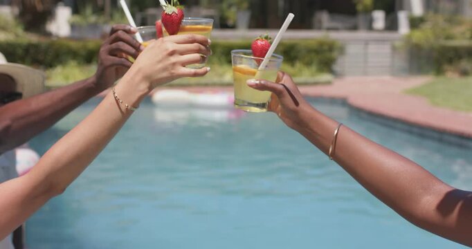 Diverse friends celebrating with straws, hands reaching in, sipping drinks poolside, copy space