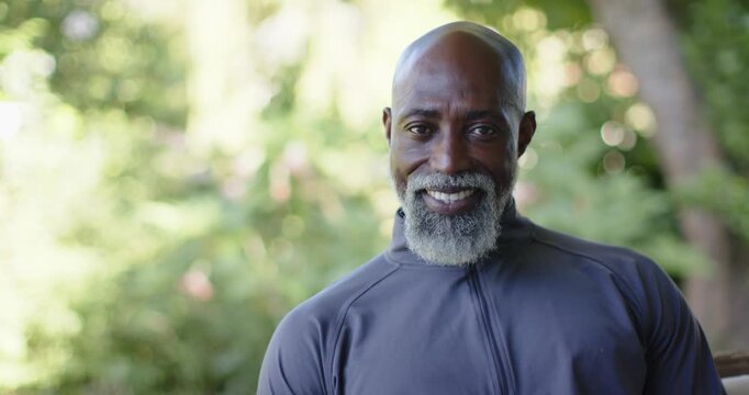 Senior African American man seeing camera, shifting gaze, smiling on porch in gray zip-up pullover