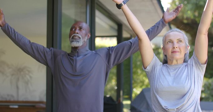 Couple doing sync arm stretch starting from T-pose on covered patio with smartwatch as home workout