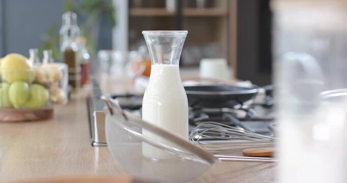 camera is panning right and pulling focus, bringing milk carafe forward for emphasis on cooktop