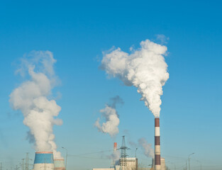 Smoking chimney releasing smoke against a blue sky. Smoke from factory pipe of heat station in the city. Air pollution. Nuclear power plant cooling. CO2, greenhouse gases emissions. CHP emissions.