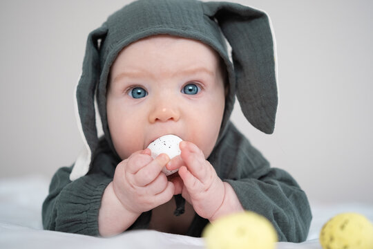 A cute boy in a bunny costume plays with colorful Easter eggs on a spring day. Funny child on Easter.