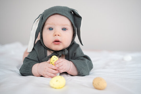 A cute boy in a bunny costume plays with colorful Easter eggs on a spring day. Funny child on Easter.