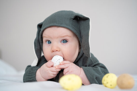 A cute boy in a bunny costume plays with colorful Easter eggs on a spring day. Funny child on Easter.