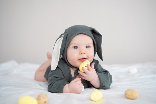 A cute boy in a bunny costume plays with colorful Easter eggs on a spring day. Funny child on Easter.