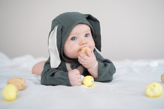 A cute boy in a bunny costume plays with colorful Easter eggs on a spring day. Funny child on Easter.