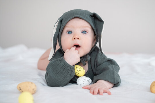 A cute boy in a bunny costume plays with colorful Easter eggs on a spring day. Funny child on Easter.