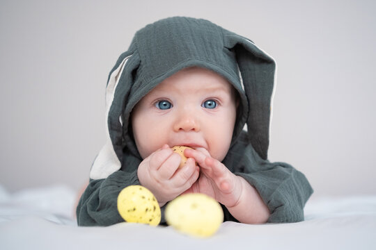 A cute boy in a bunny costume plays with colorful Easter eggs on a spring day. Funny child on Easter.