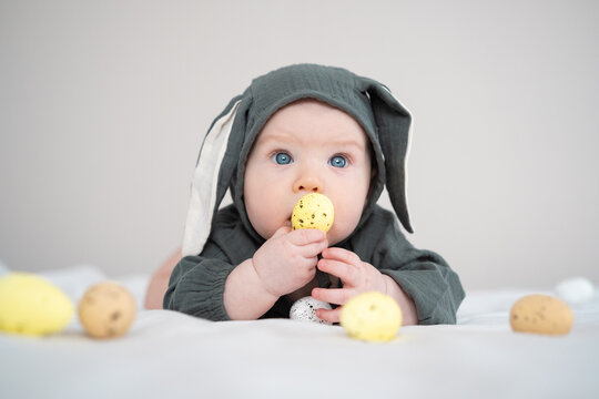 A cute boy in a bunny costume plays with colorful Easter eggs on a spring day. Funny child on Easter.