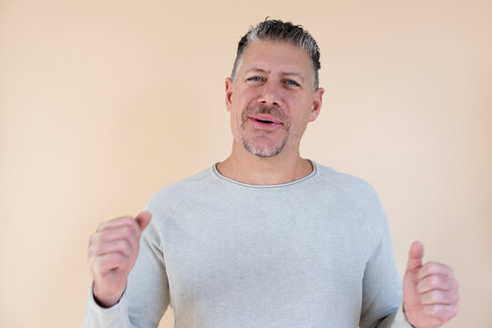 Man with gray hair and brown sweater standing in front of brown background